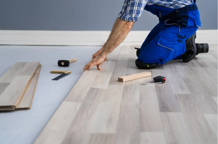 A person in blue overalls kneeling on the floor with a hammer and a piece of wood AI-generated content may be incorrect.